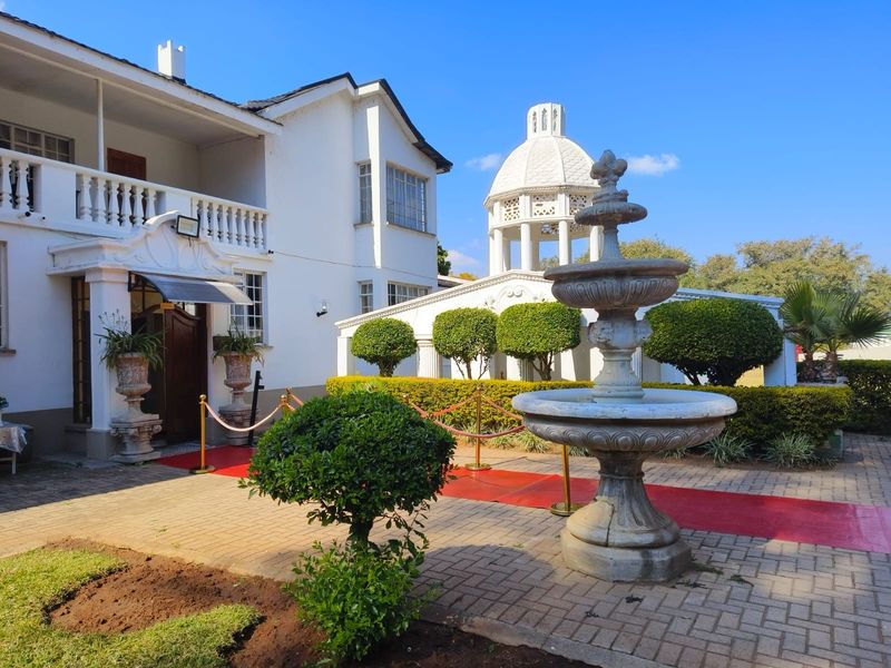 A well-maintained lodge entrance featuring a classic stone fountain, paved courtyard, and a distinctive domed gazebo structure set against the main building facade.
