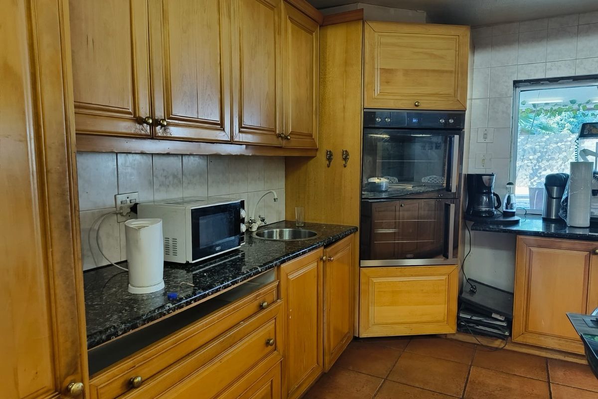 A functional kitchen featuring wooden cabinetry, granite countertops, a built-in double oven, and tiled flooring, offering a traditional aesthetic with potential for modernization.