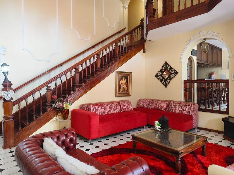 Spacious living area featuring a grand wooden staircase, decorative wall molding, and classic checkered floor tiles, leading into an adjacent bar area.