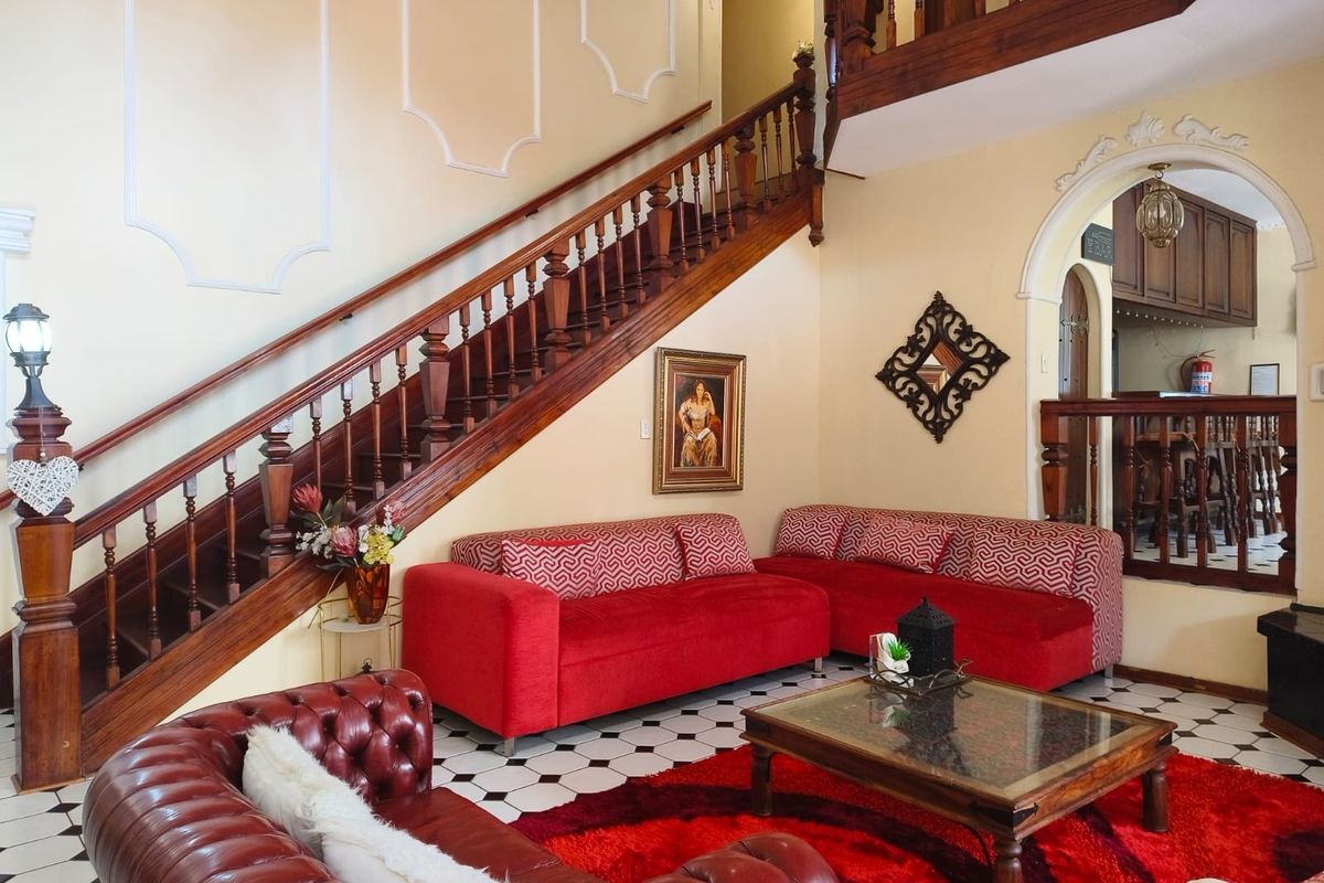 Spacious living area featuring a grand wooden staircase, decorative wall molding, and classic checkered floor tiles, leading into an adjacent bar area.