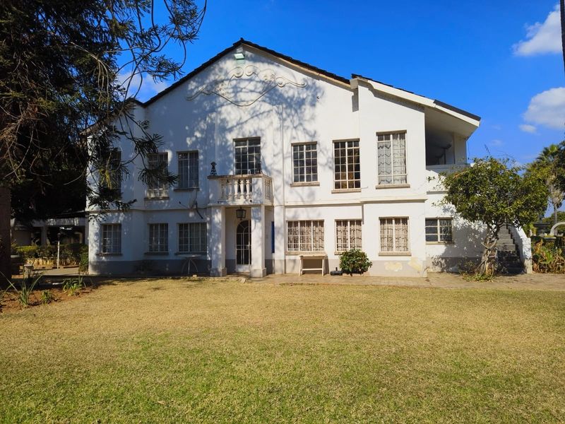 Rear elevation of a multi-story lodge featuring a paved patio, balcony, and classic multi-pane windows set against a large lawn area.