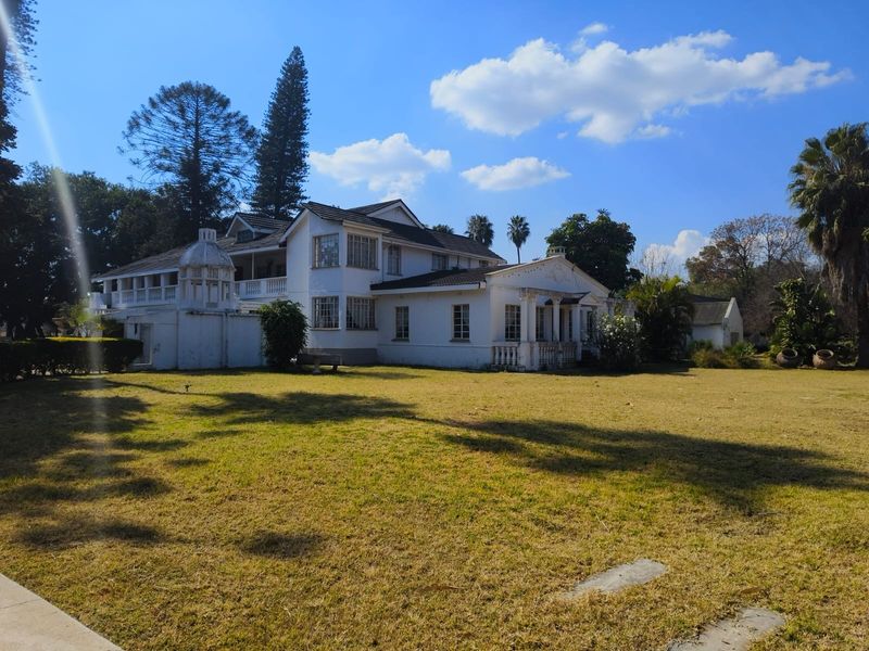 A spacious rear view of the lodge featuring a large lawn, classic architectural columns, a balcony, and a distinctive cupola structure.