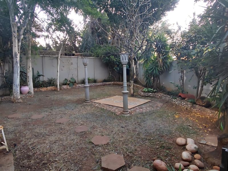 A private rear garden featuring a perimeter wall, mature trees, and a central paved area with decorative pillars.