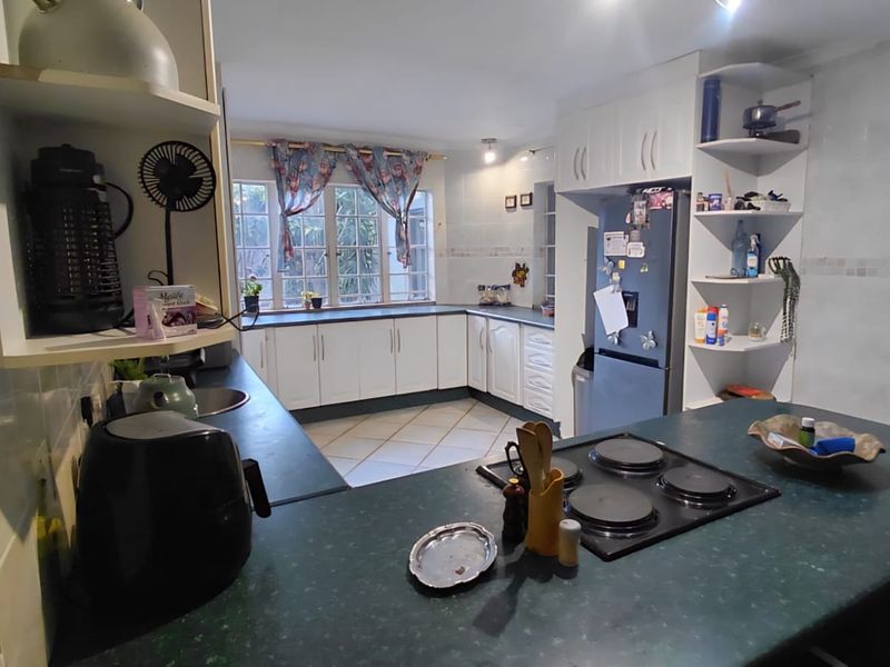 A functional kitchen featuring white cabinetry, dark laminate countertops, an integrated electric hob, and tiled flooring with ample storage space.