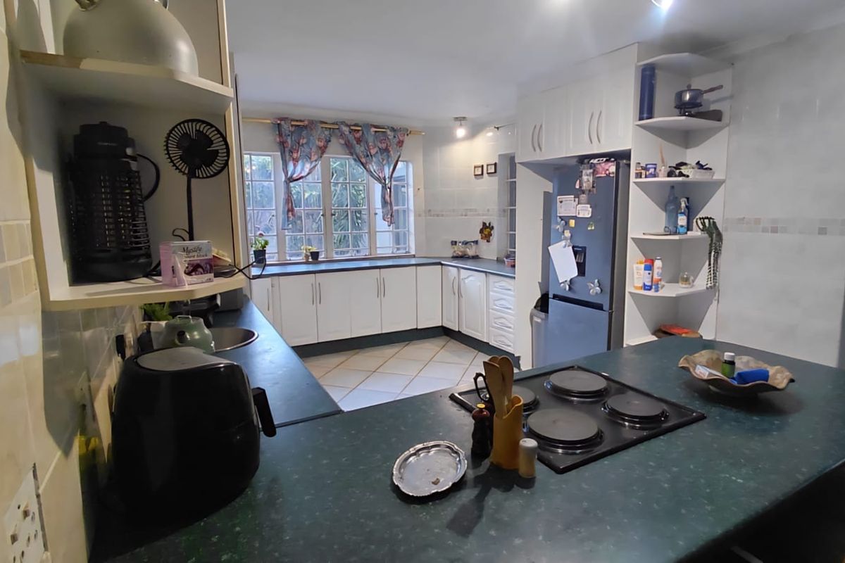 A functional kitchen featuring white cabinetry, dark laminate countertops, an integrated electric hob, and tiled flooring with ample storage space.