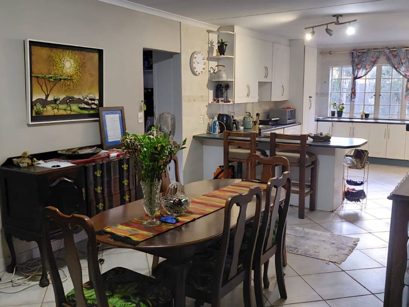 Open plan kitchen and dining area featuring tiled flooring, white cabinetry, a breakfast bar, and ample natural light from the rear window.