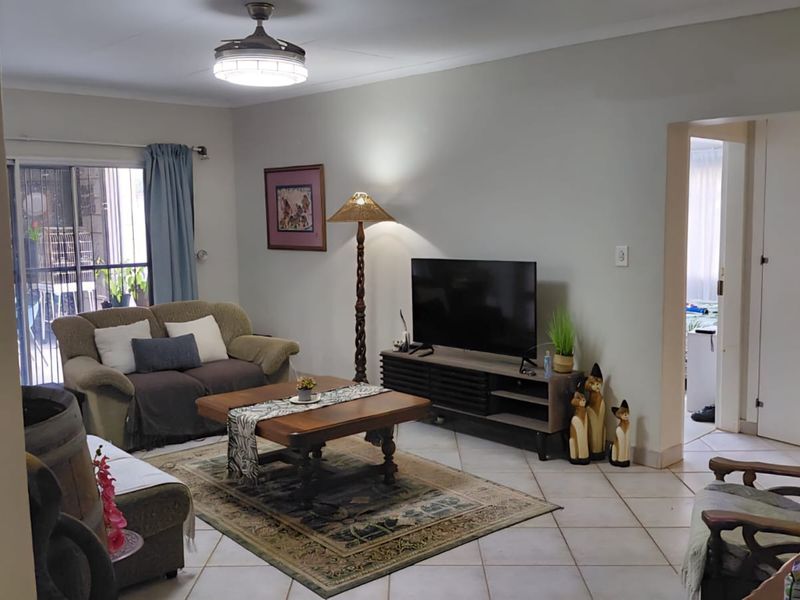 A comfortable living room featuring tiled flooring, a ceiling fan, and a sliding glass door providing access to the exterior.