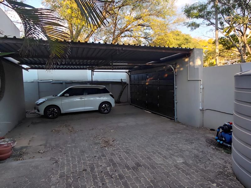 A covered carport area featuring a sectional garage door, paved flooring, and an external water storage tank.