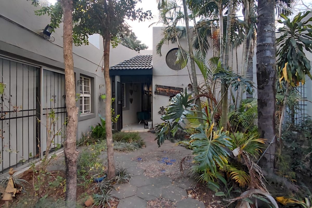 A private rear courtyard area featuring a paved walkway, established garden landscaping, and direct access to the home through security-gated sliding doors.