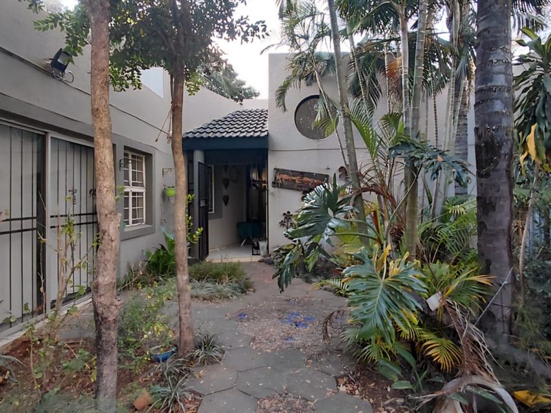 A private rear courtyard area featuring a paved walkway, established garden landscaping, and direct access to the home through security-gated sliding doors.