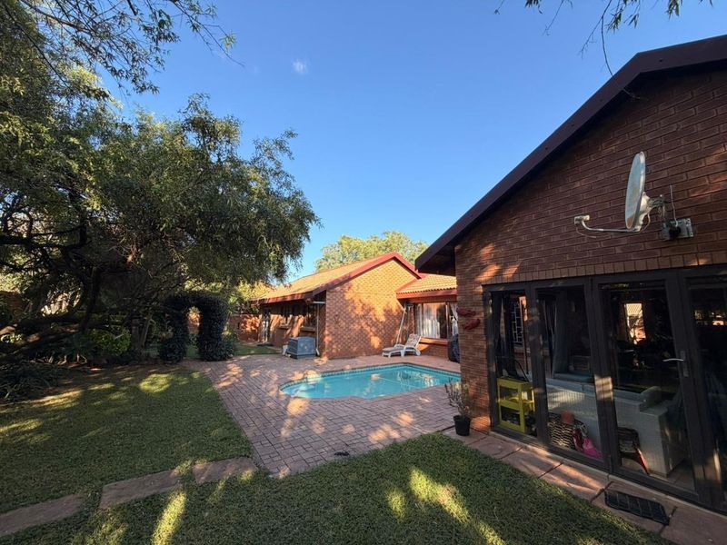 Rear exterior view featuring a swimming pool, brick paved patio area, and established garden surroundings with direct access to the home via sliding doors.