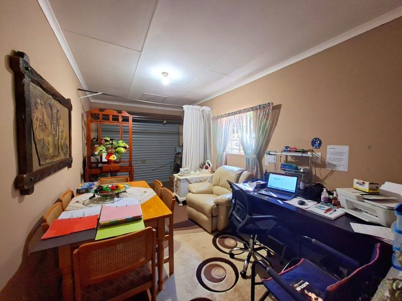A converted garage space currently utilized as a multi-purpose room, featuring a roller shutter door, coved ceiling, and security-barred window.