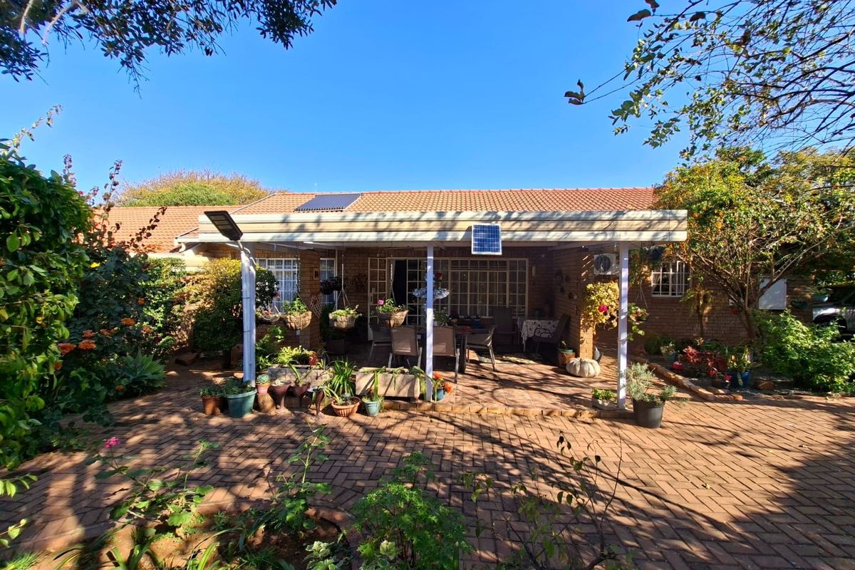 A rear view of the townhouse featuring a covered patio area, brick paving, and a well-established garden setting.