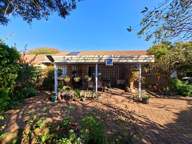 A rear view of the townhouse featuring a covered patio area, brick paving, and a well-established garden setting.