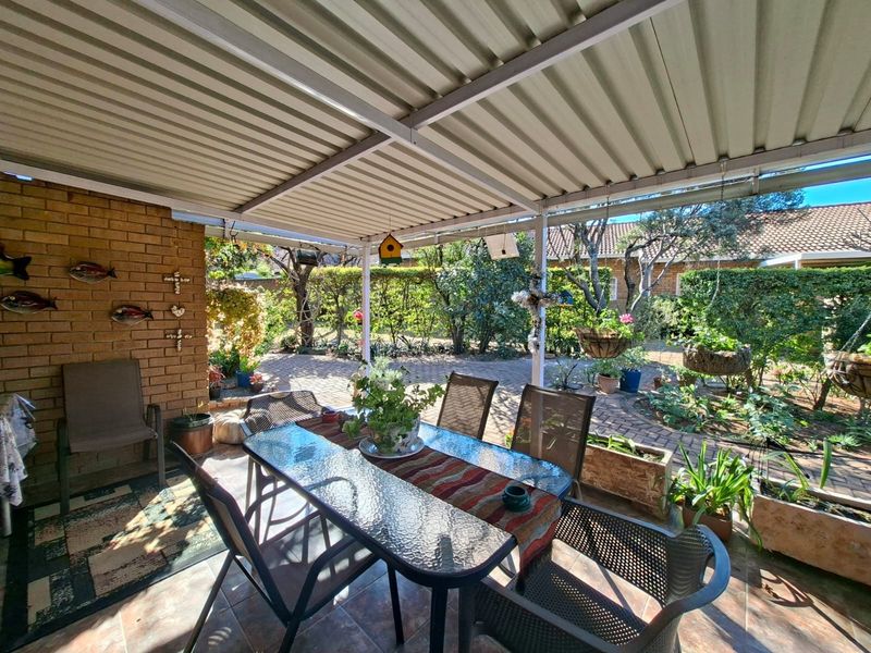 A covered outdoor patio area featuring a corrugated metal roof, brick wall accents, and tiled flooring, overlooking a landscaped garden.