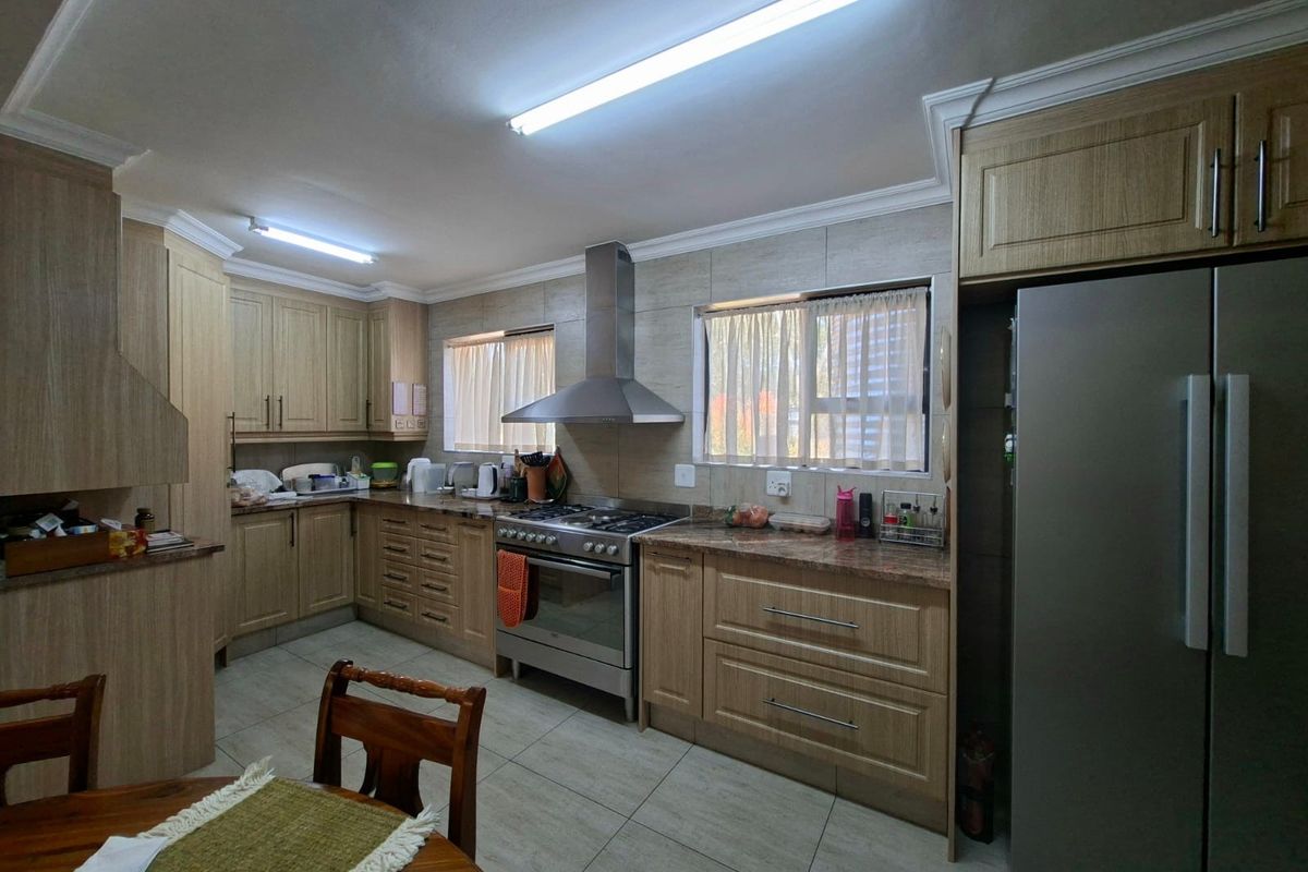 A functional kitchen featuring wood-finish cabinetry, granite countertops, a stainless steel gas stove with extractor fan, and tiled flooring.
