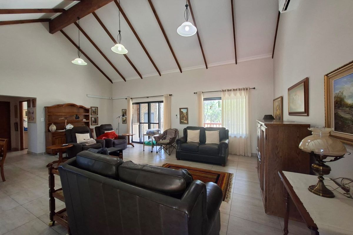 Spacious living room featuring a high vaulted ceiling with exposed timber beams, tiled flooring, and large sliding glass doors providing natural light.