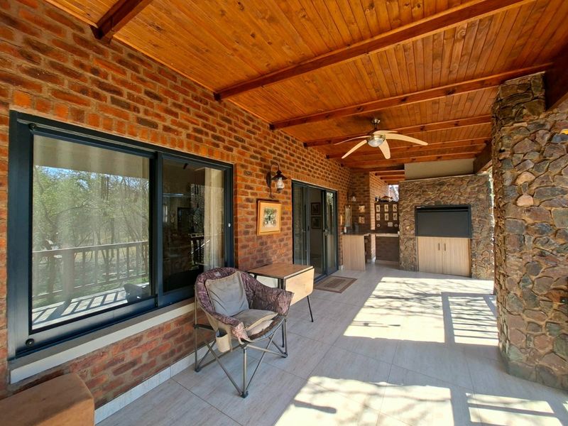 Covered patio featuring exposed brickwork, a timber ceiling, stone-clad built-in braai, and tiled flooring, providing an ideal space for outdoor entertaining.