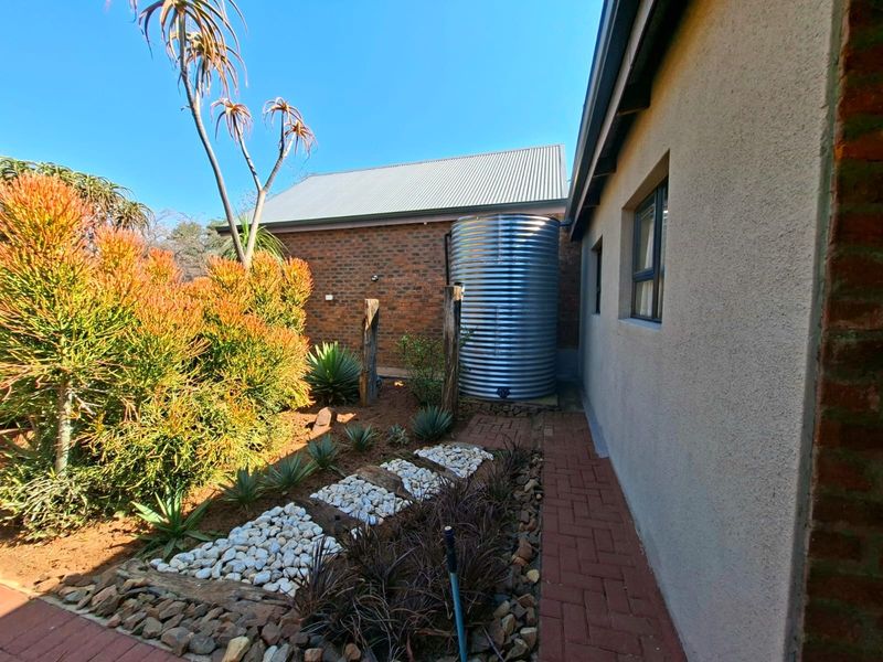 A well-maintained rear garden area featuring a corrugated metal water tank, brick paving, and established landscaping alongside the house exterior.