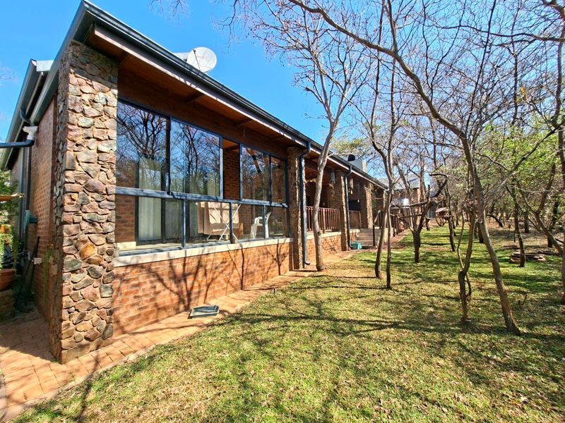 Rear view of the house featuring stone and brick exterior, large glass windows, and a covered patio area overlooking the garden.