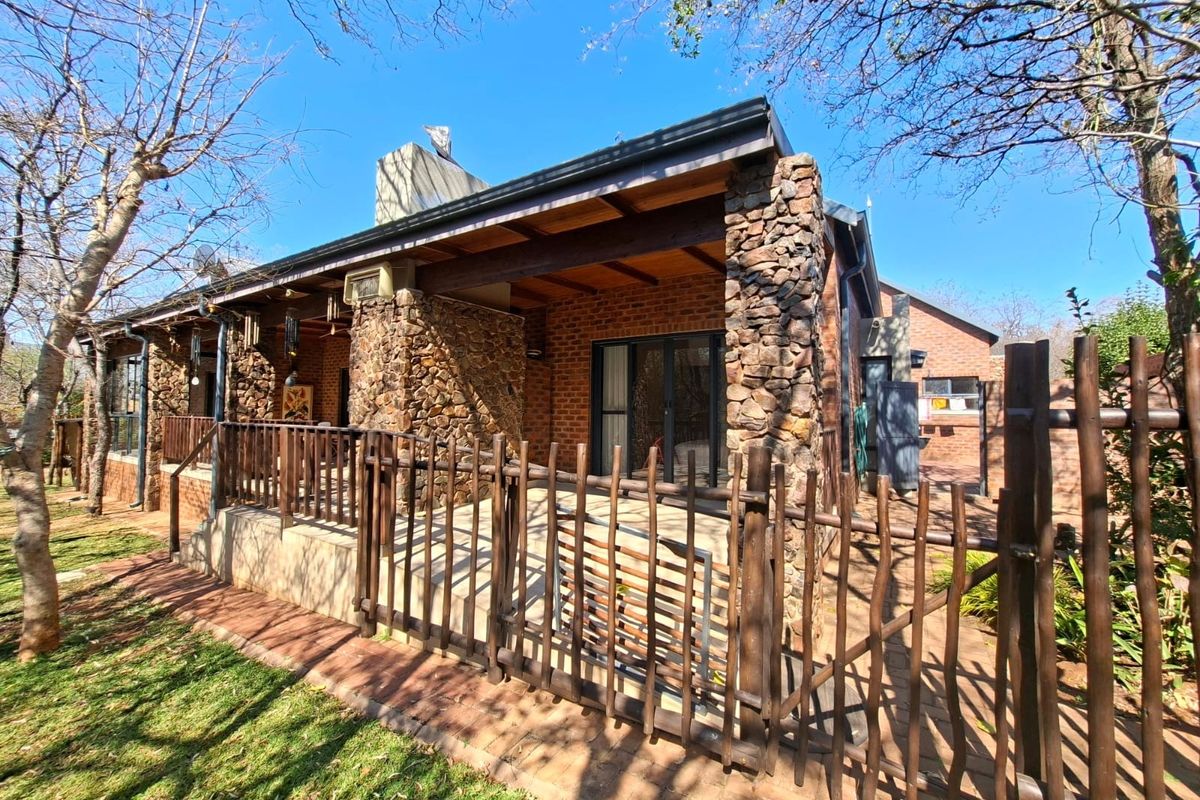 Rear view of the house featuring a covered patio with stone pillars, brick walls, and timber accents, overlooking a landscaped garden area.