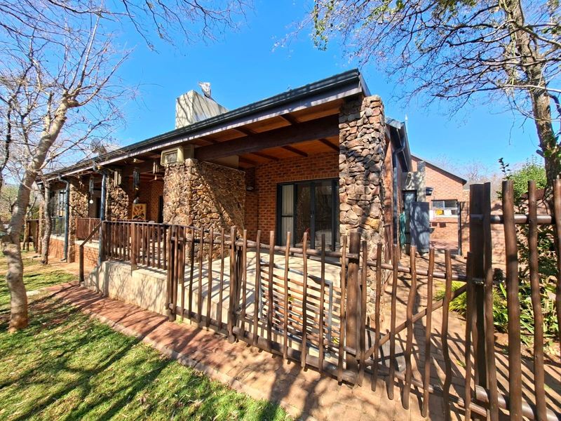 Rear view of the house featuring a covered patio with stone pillars, brick walls, and timber accents, overlooking a landscaped garden area.