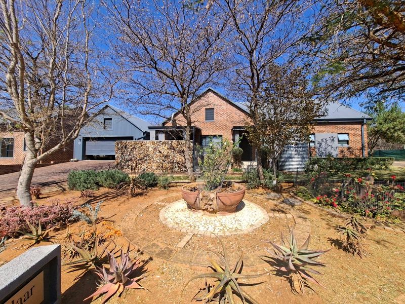 Front view of a charming brick house featuring a landscaped garden, stone feature wall, and an attached garage.