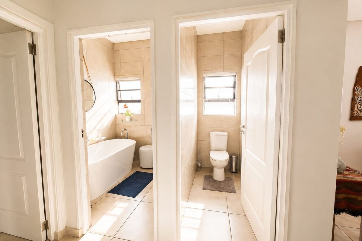 A bright bathroom featuring a freestanding bathtub in one section and a separate toilet area, both finished with neutral wall and floor tiles.