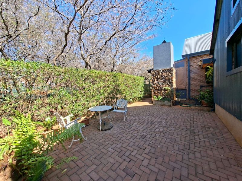 A private outdoor patio area featuring brick paving, a stone-clad chimney, and established hedge landscaping, providing a cozy space for outdoor relaxation.