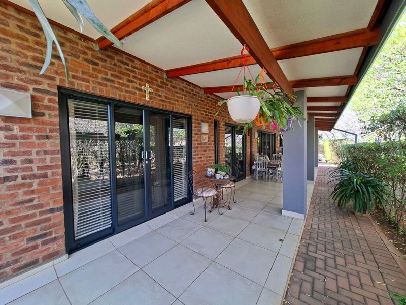 A covered patio featuring exposed timber beams, tiled flooring, and brick wall finishes, providing direct access to the home through sliding glass doors.
