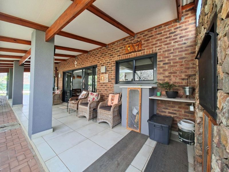 A covered patio area featuring exposed timber beams, tiled flooring, and a combination of brick and stone wall finishes with sliding door access.