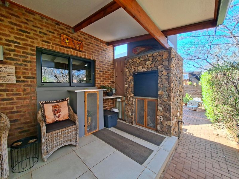 Covered outdoor patio featuring a built-in braai with stone cladding, exposed brick walls, and tiled flooring, ideal for outdoor entertaining.