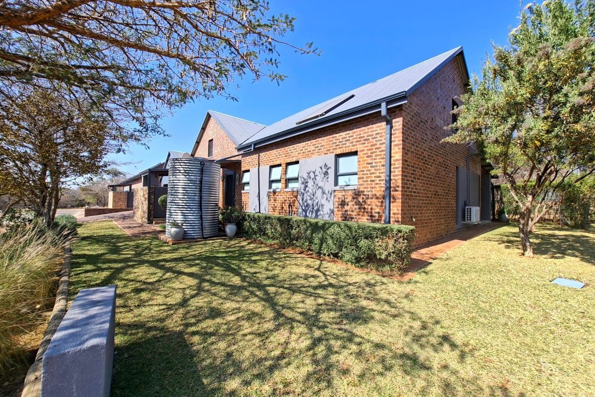 A well-maintained brick house exterior featuring a metal roof, solar panels, a water tank, and a neat garden area.