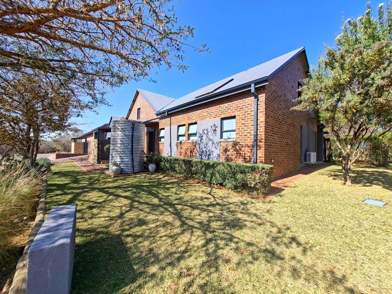 A well-maintained brick house exterior featuring a metal roof, solar panels, a water tank, and a neat garden area.