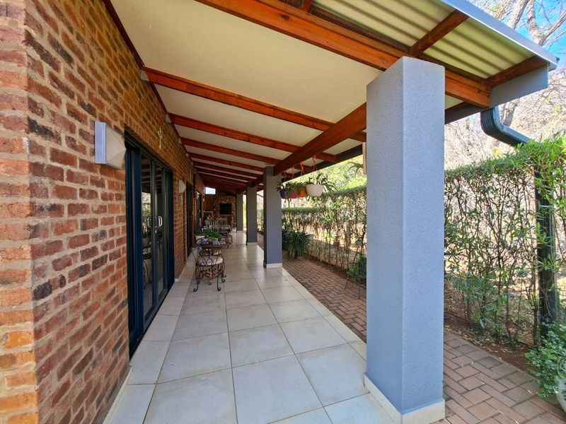 A covered outdoor patio featuring tiled flooring, exposed timber rafters, and brick wall detailing, providing a seamless transition to the garden area.