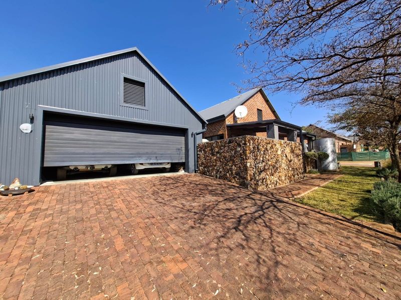 Front view of the property featuring a modern corrugated metal garage, stone gabion wall, and a brick paved driveway.