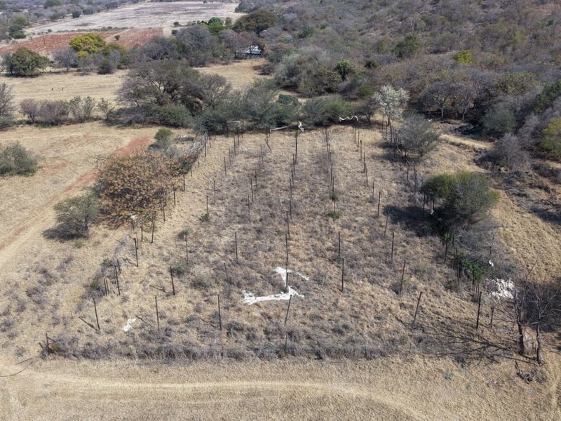 Aerial view of a fenced agricultural plot on a farm, showing dry terrain and damaged perimeter fencing.