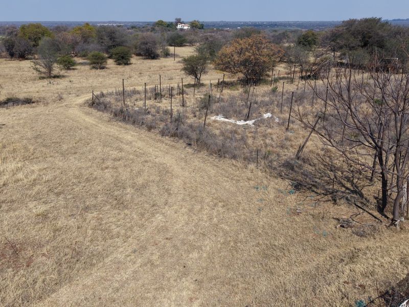 An aerial view of a rural farm property featuring dry grassland, a dirt access track, and perimeter wire fencing.