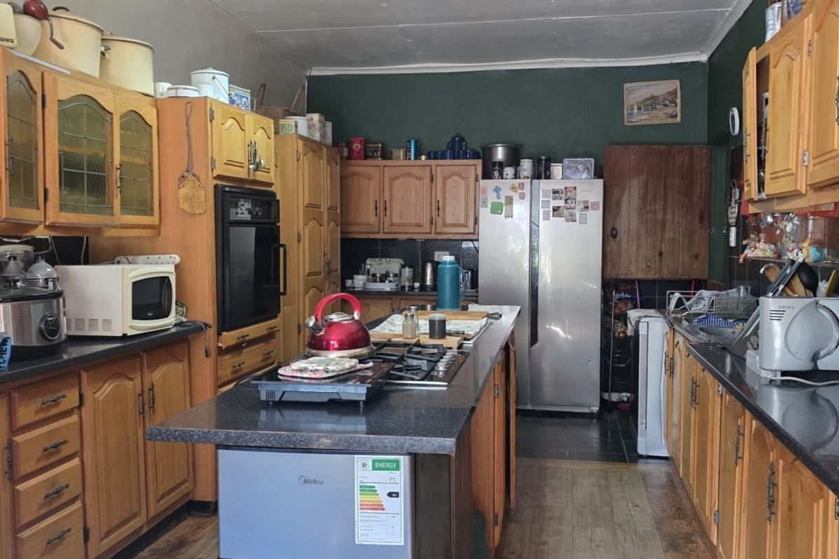 A functional kitchen featuring extensive wooden cabinetry, granite countertops, a central island with a gas hob, and built-in oven appliances.