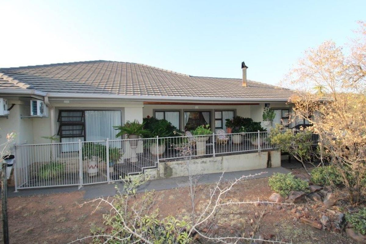 Rear view of the house featuring a tiled roof, a raised concrete patio with metal balustrading, and multiple sliding door access points.