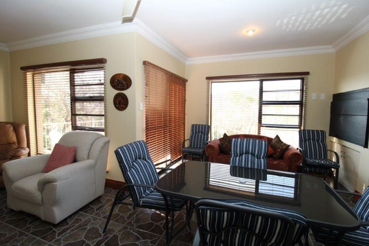 A living area featuring tiled flooring, crown molding, and large windows with venetian blinds, offering a functional space with natural light.