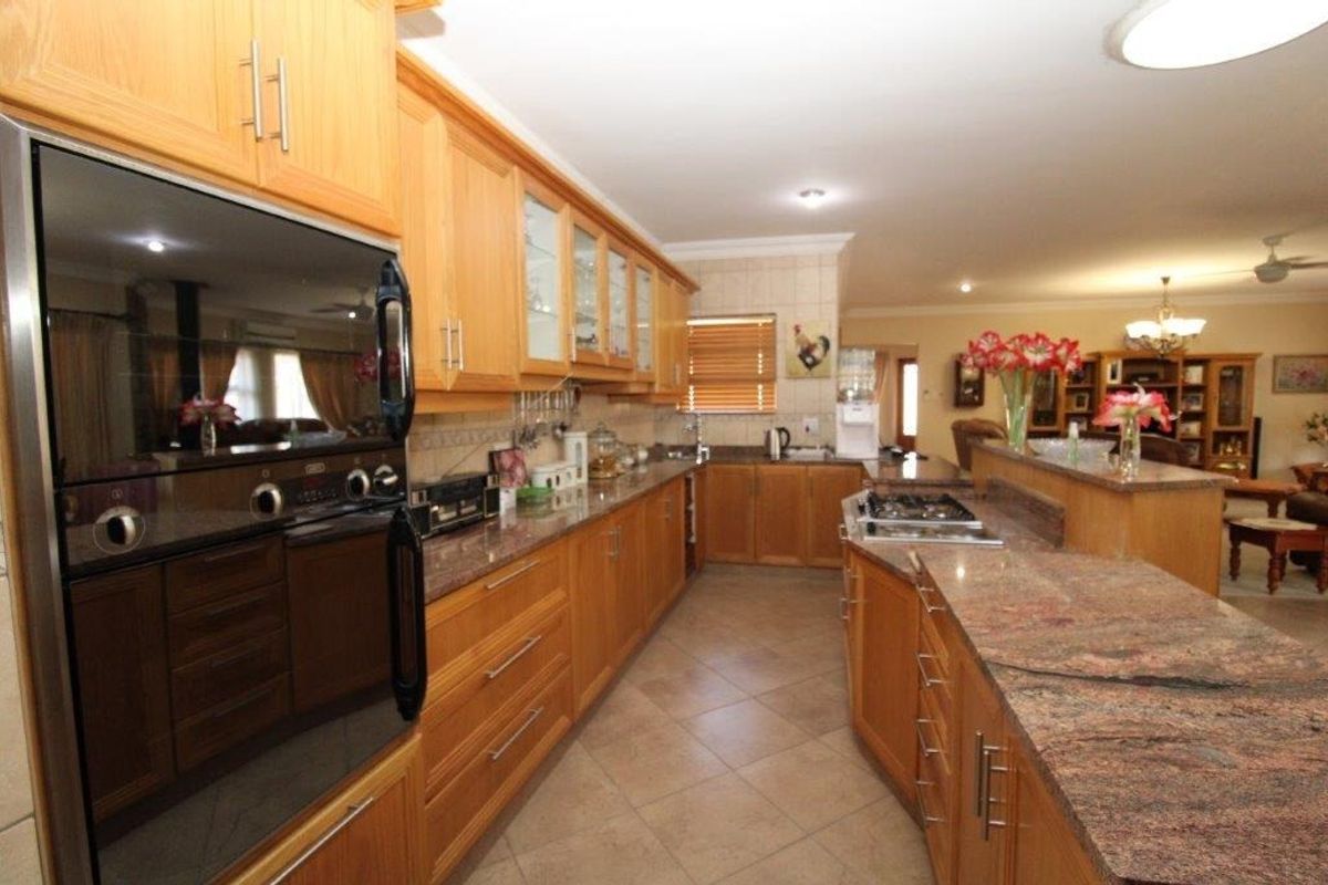 Spacious kitchen featuring warm wooden cabinetry, granite countertops, built-in oven, gas hob, and tiled flooring, flowing into an open-plan living area.