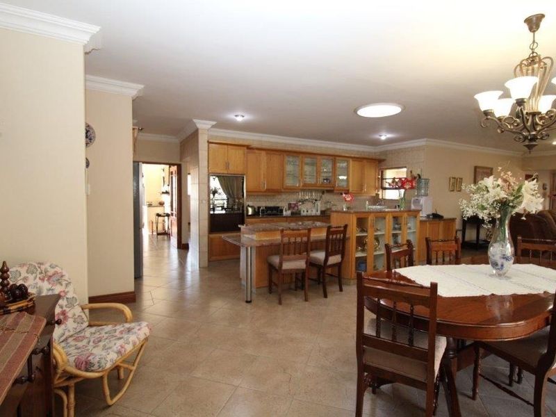 Spacious open-plan kitchen and dining area featuring wooden cabinetry, granite countertops, a central island, and tiled flooring throughout.
