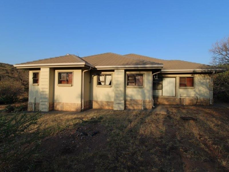 Rear elevation of a single-story house featuring a tiled roof, stone cladding base, and multiple casement windows set in a natural landscape.