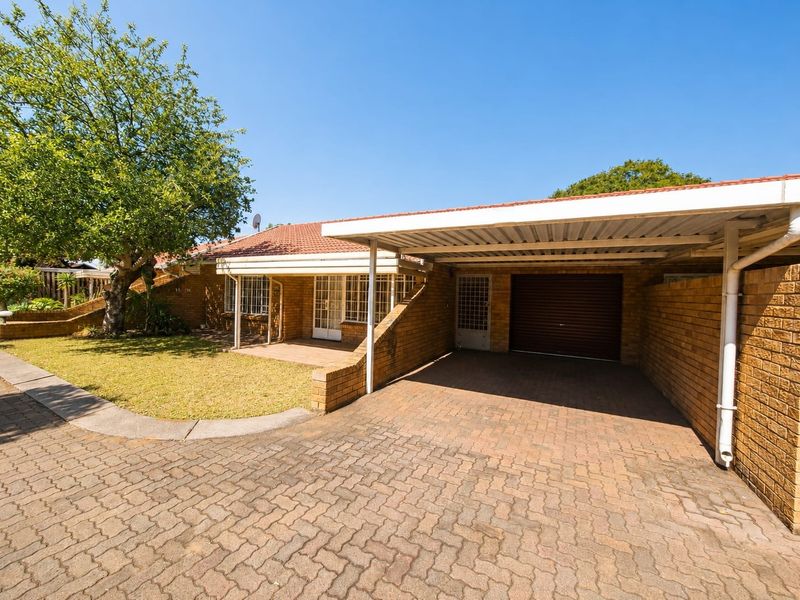 Front exterior view of a brick retirement village unit featuring a paved driveway, covered carport, and secure entrance.