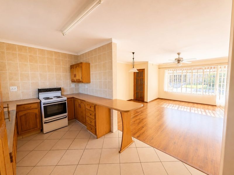 Open-plan kitchen and living area featuring wooden cabinetry, tiled splashbacks, laminate flooring, and a ceiling fan, offering a functional and bright living space.
