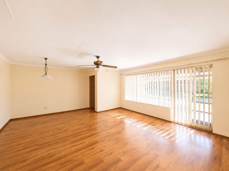 Spacious, empty living room featuring laminate flooring, a ceiling fan, and large sliding glass doors with vertical blinds providing natural light.