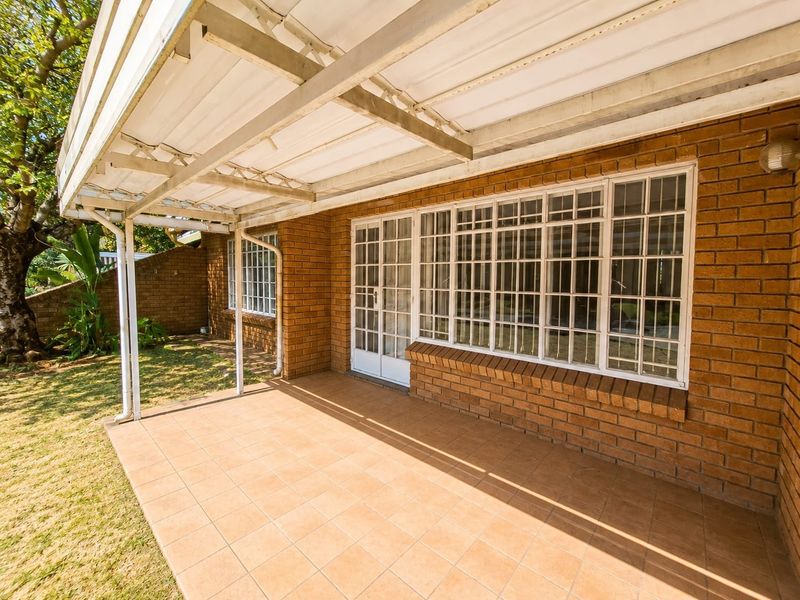 A covered outdoor patio area featuring tiled flooring, brick exterior walls, and direct access to the interior through glass sliding doors.
