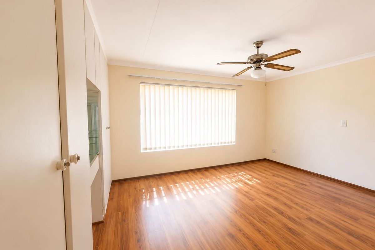A bright, empty bedroom featuring laminate flooring, built-in cupboards, and a ceiling fan, offering a clean and neutral space ready for personalization.