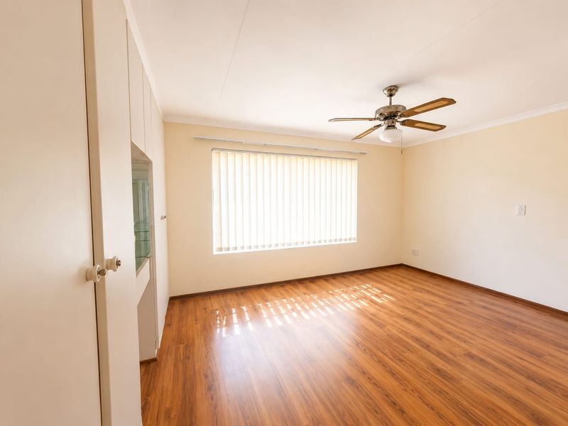 A bright, empty bedroom featuring laminate flooring, built-in cupboards, and a ceiling fan, offering a clean and neutral space ready for personalization.